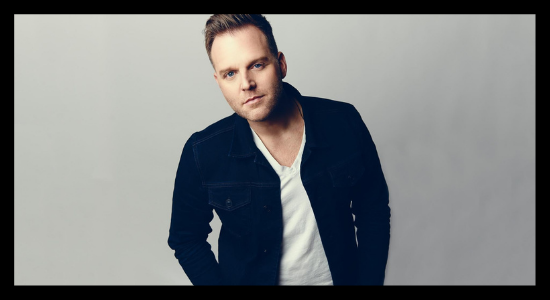 Matthew West wears a black jacket and white t shirt standing in front of a grey background